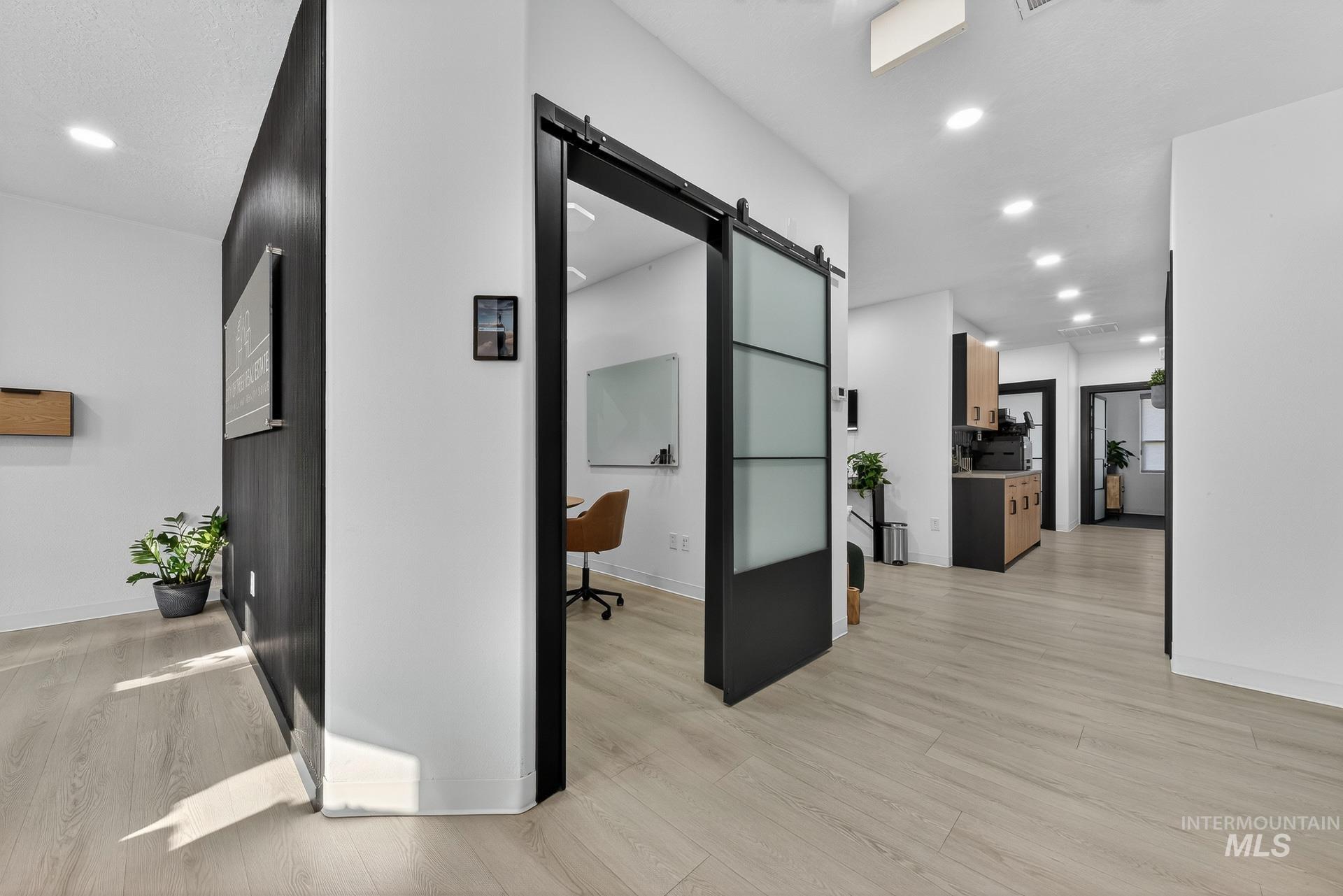 Hallway with a barn door, an office area, recessed lighting, and light wood-type flooring