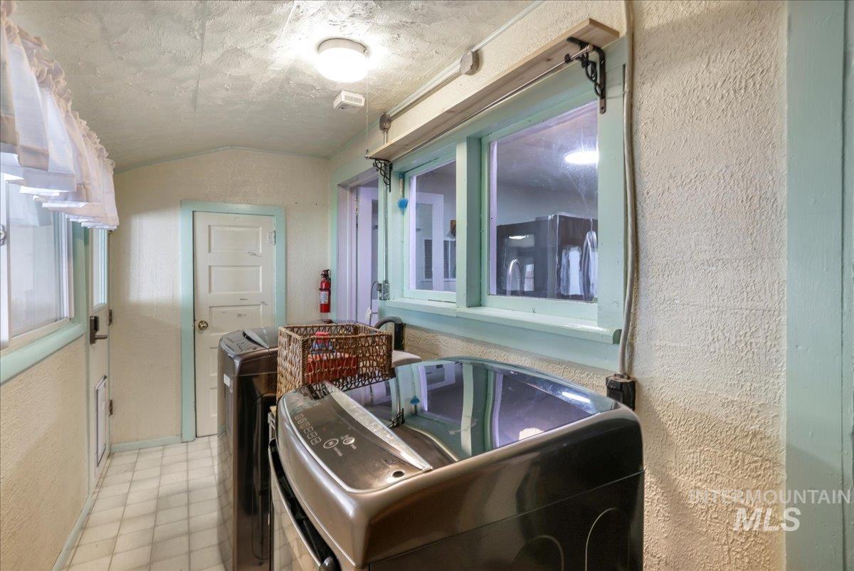 Bathroom with washer and clothes dryer, a textured wall, vaulted ceiling, and tile patterned flooring