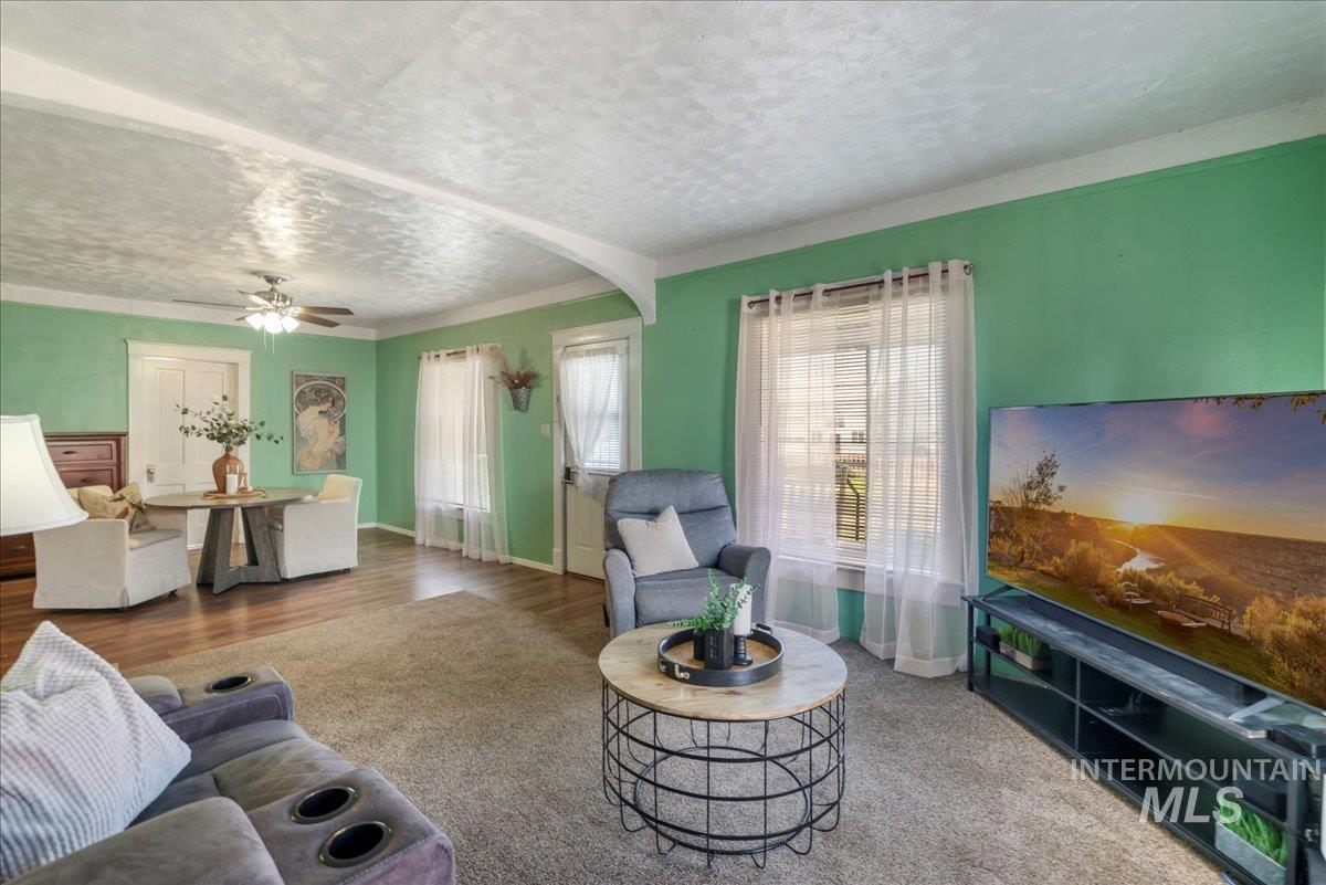 Living room with a textured ceiling, a ceiling fan, and wood finished floors