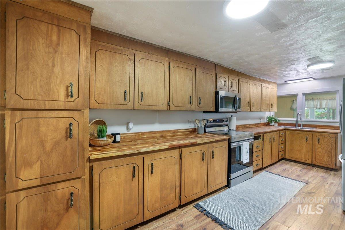 Kitchen featuring appliances with stainless steel finishes, light wood-style flooring, wood counters, and brown cabinetry