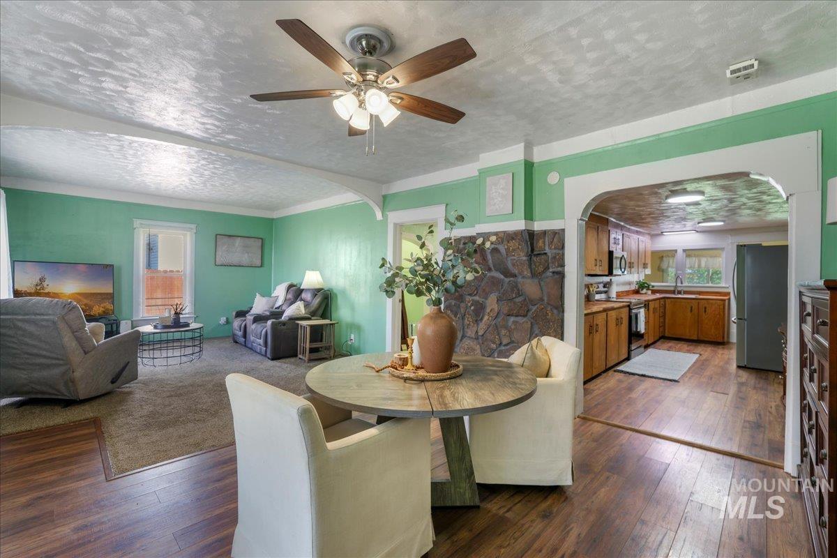 Dining space with arched walkways, a ceiling fan, dark wood-type flooring, and a textured ceiling