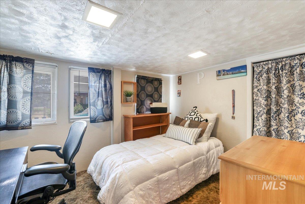 Bedroom with dark carpet, a textured ceiling, and a desk