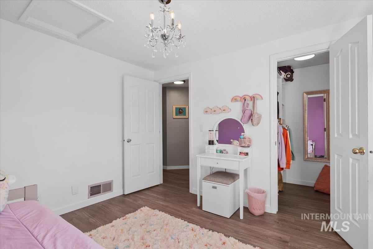 Bedroom featuring dark wood-style flooring, a textured ceiling, attic access, and a chandelier