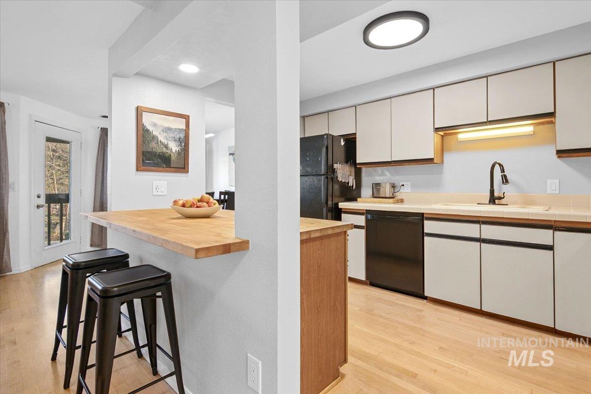 Kitchen featuring light wood finished floors, a breakfast bar area, black appliances, and butcher block countertops