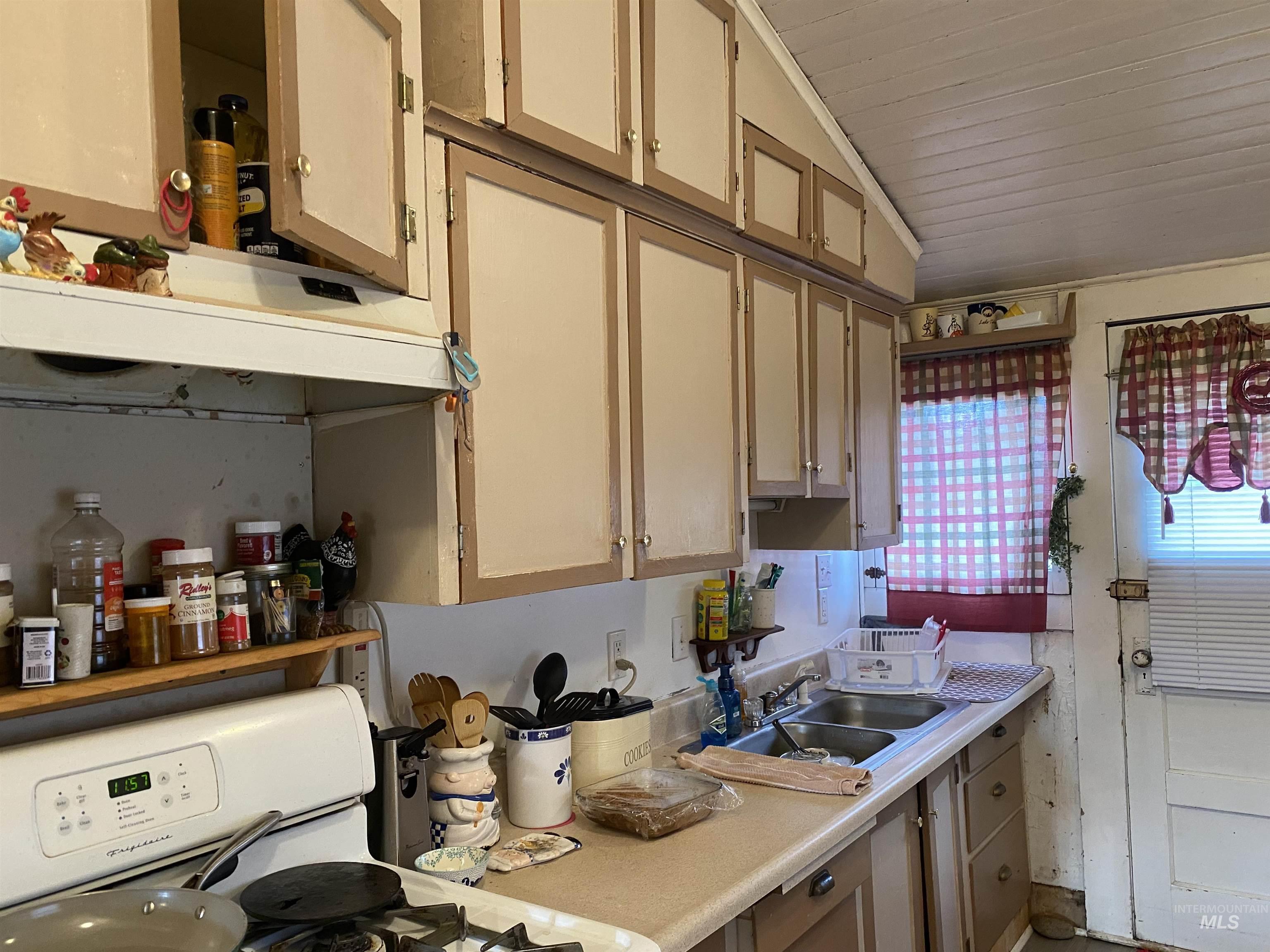 Kitchen with gas range gas stove, vaulted ceiling, light countertops, light brown cabinets, and under cabinet range hood