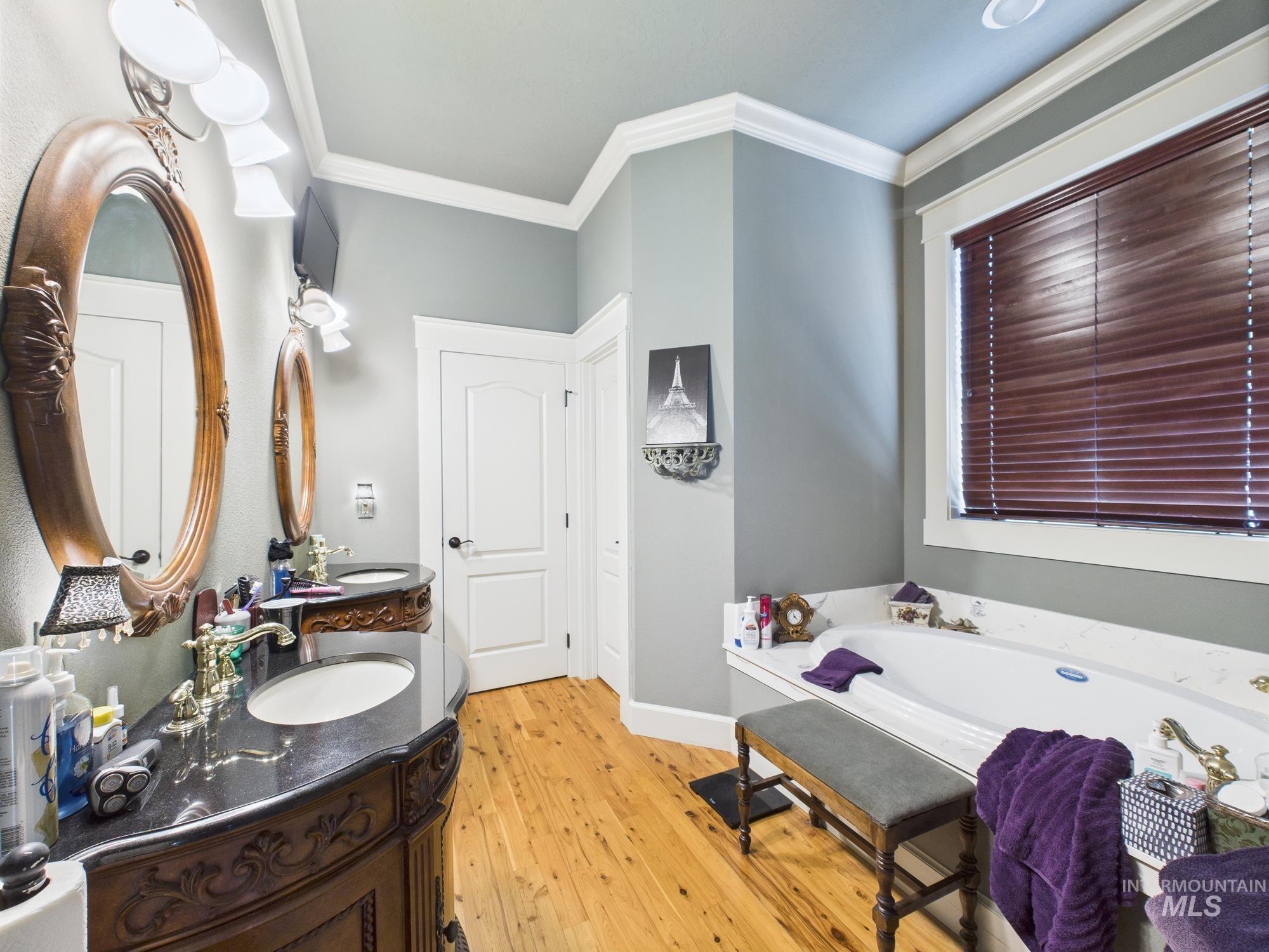 Bathroom with wood finished floors, vanity, crown molding, and a bath