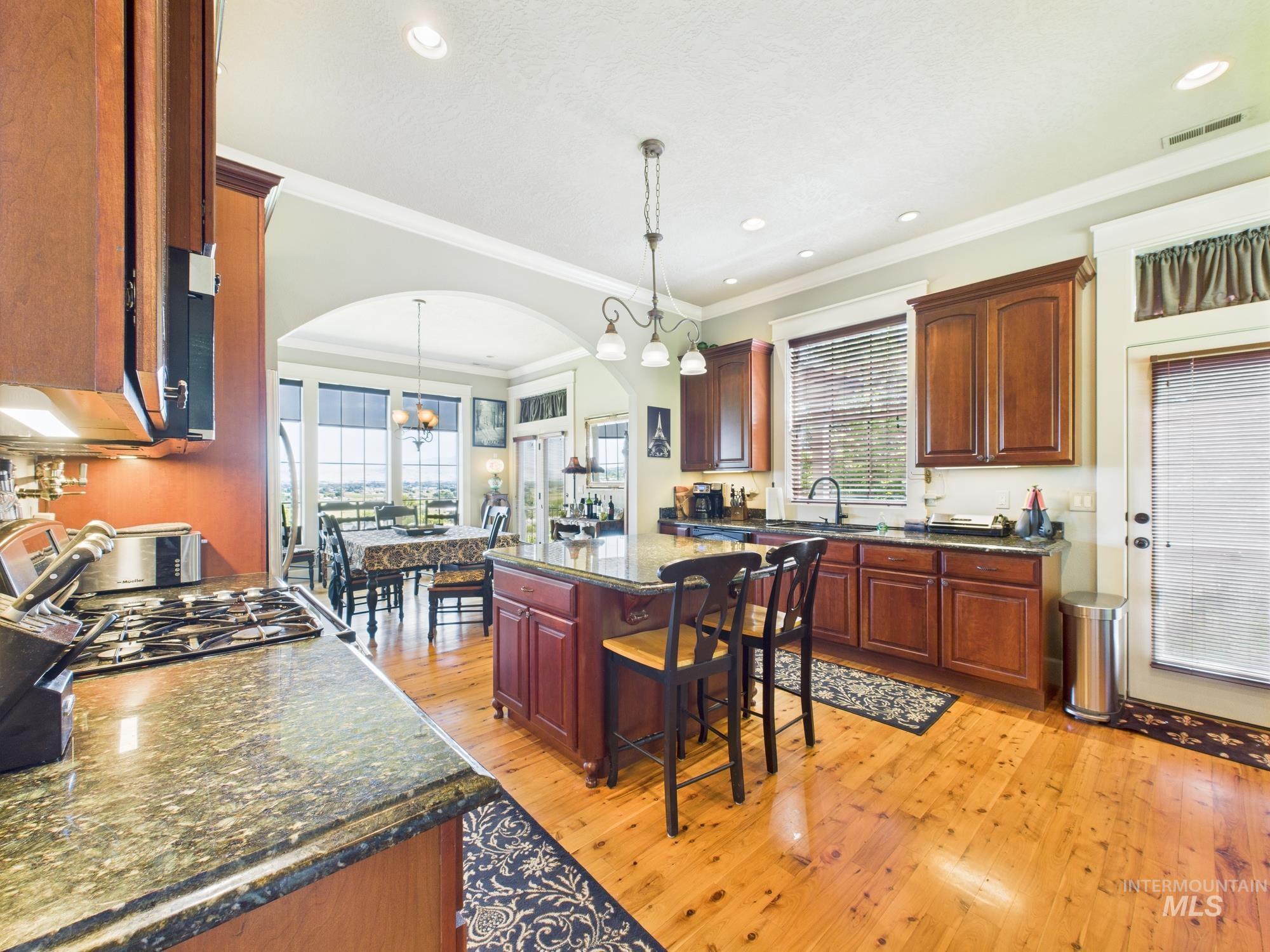 Kitchen featuring arched walkways, light wood-style floors, a breakfast bar, crown molding, and pendant lighting