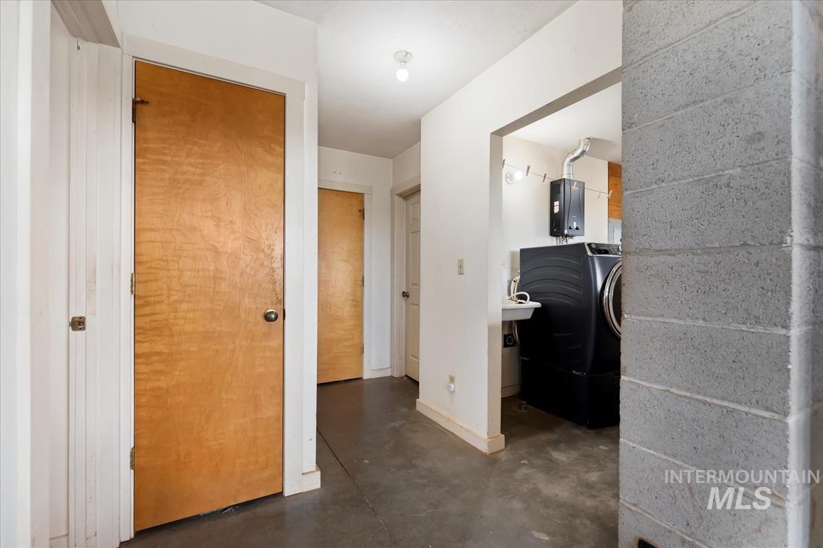 Hallway with washer / dryer, concrete flooring, and concrete block wall