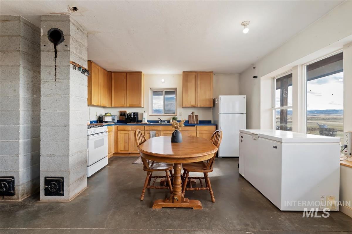Kitchen with white appliances, concrete floors, dark countertops, and light brown cabinetry