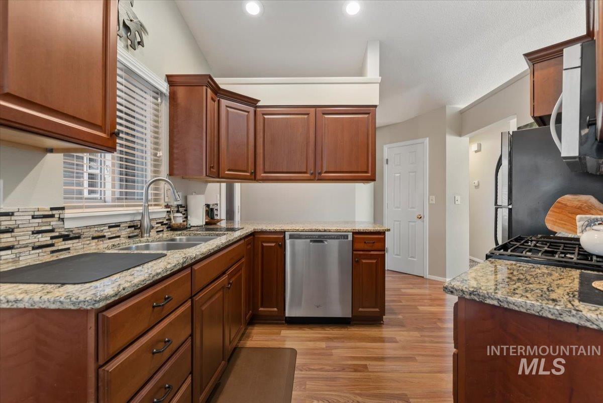 Kitchen featuring light wood-style floors, stainless steel appliances, granite countertops, wood finish cabinetry, and recessed lighting
