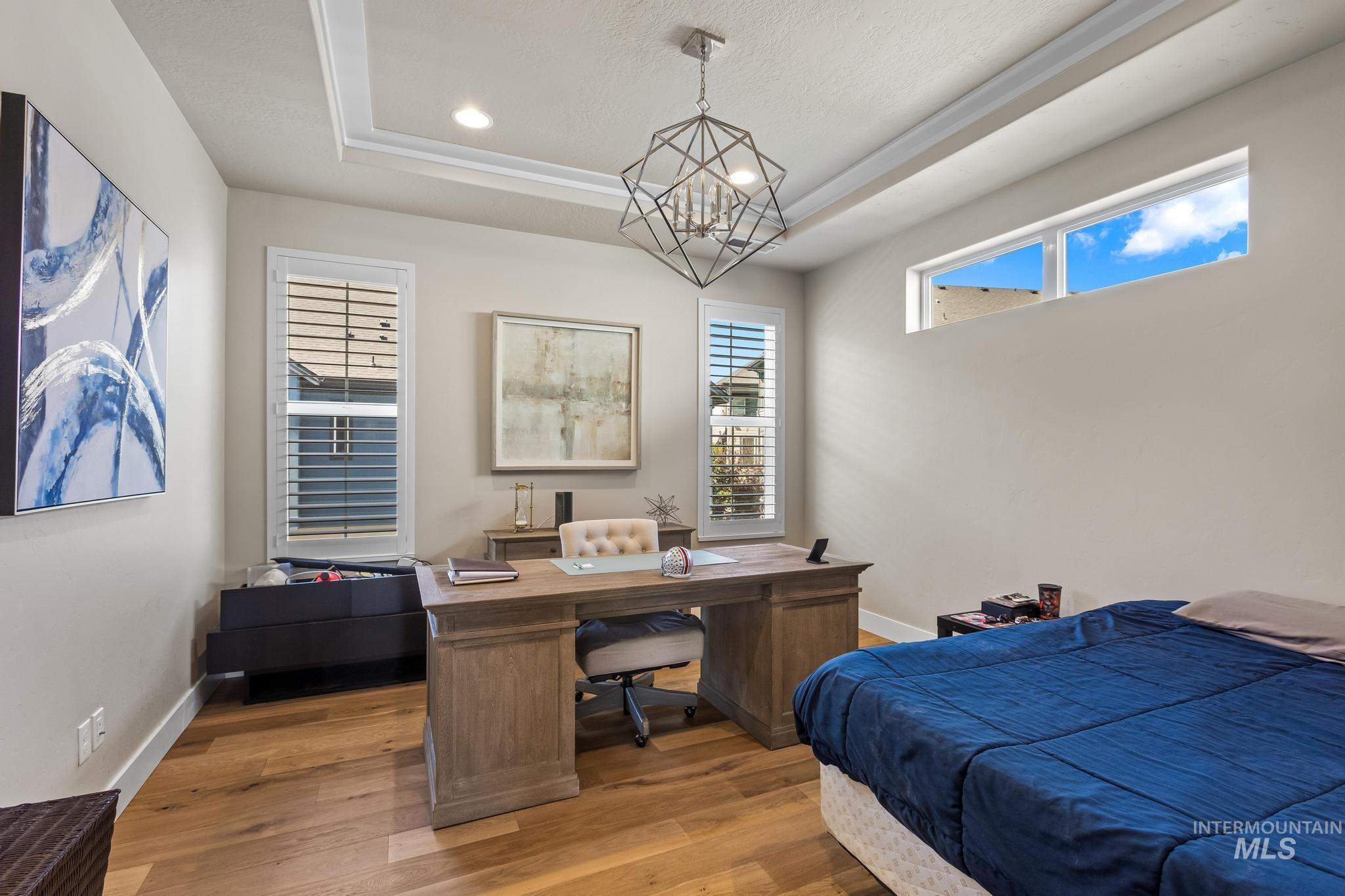 Bedroom with a raised ceiling, wood finished floors, recessed lighting, and a chandelier
