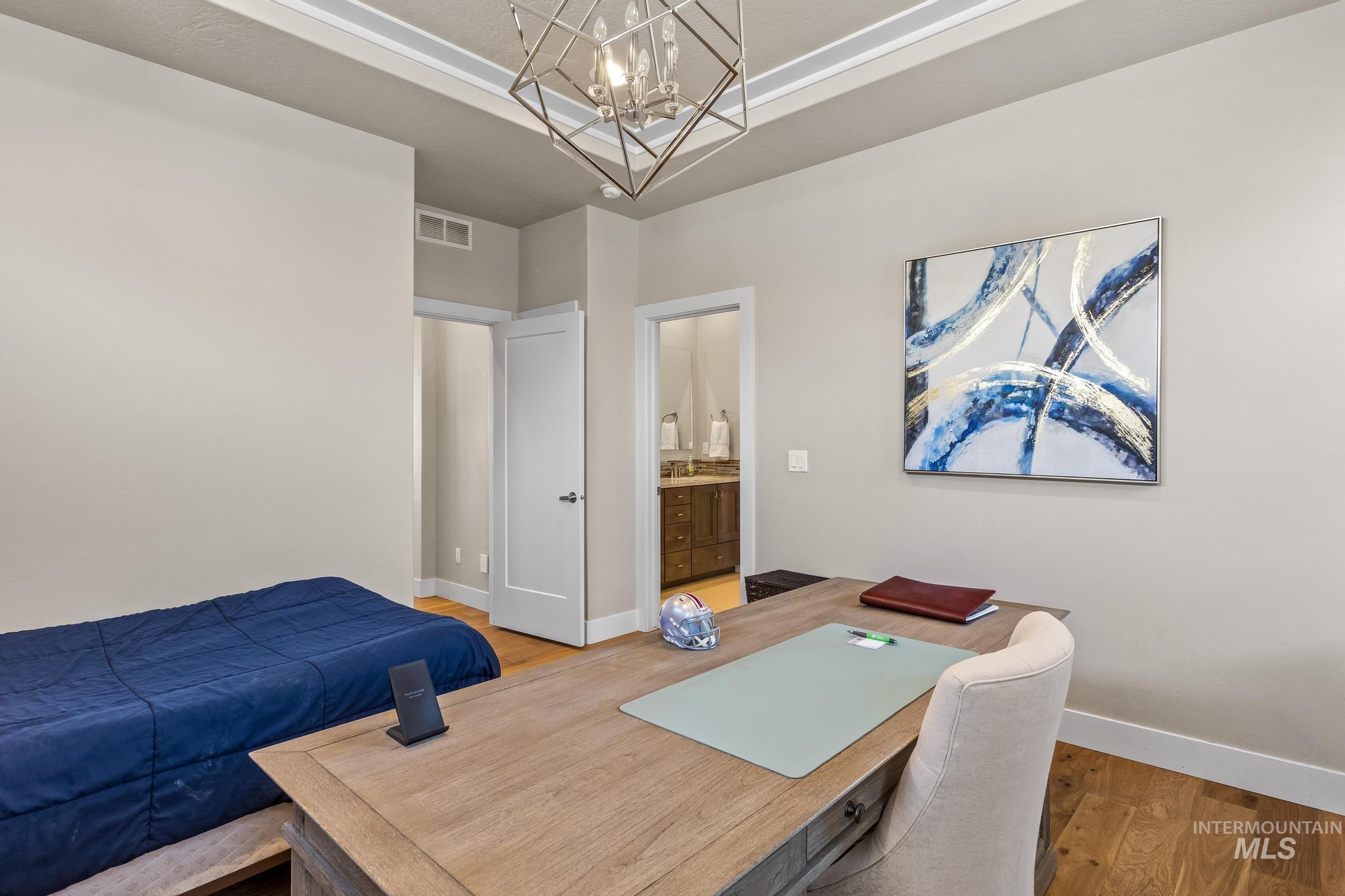 master bedroom featuring wood finished floors, a raised ceiling, and a chandelier