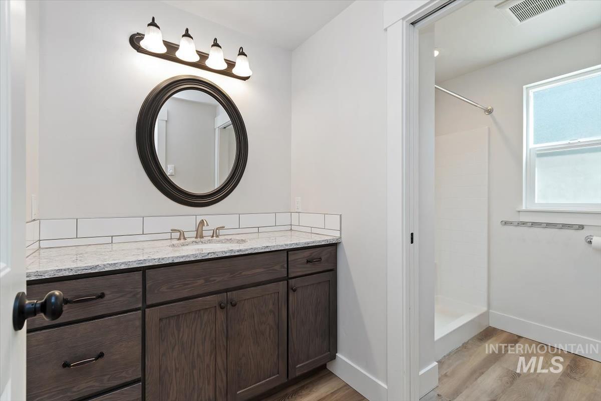 Bathroom featuring a dark wood-finish vanity with a light-toned countertop, a round framed mirror, and a four-light fixture
