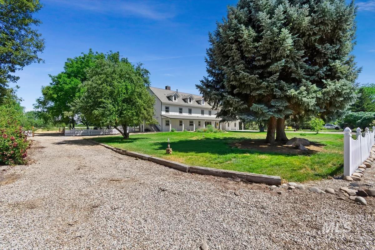 Exterior property featuring a gravel driveway, mature trees, manicured lawn, and white picket fencing