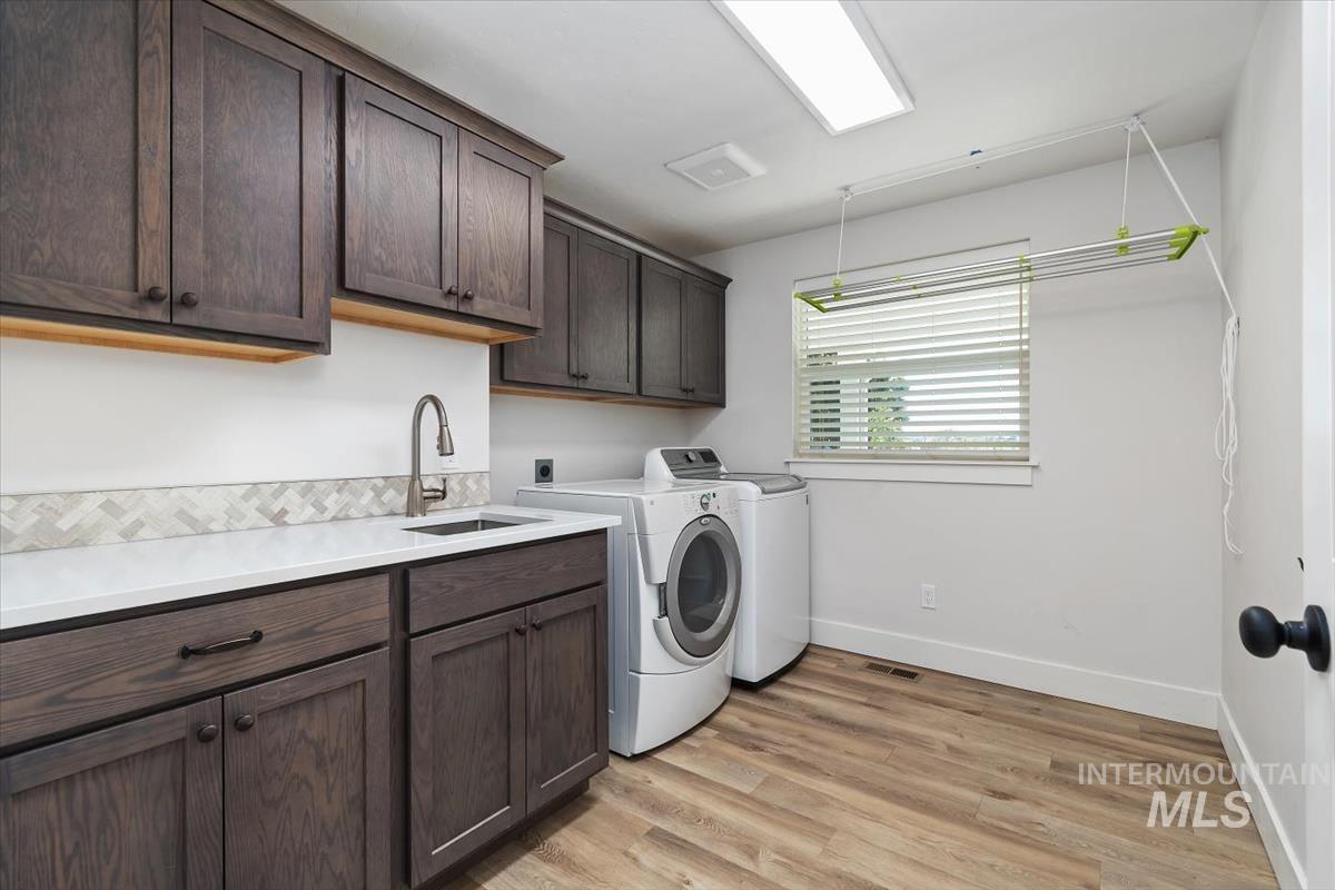Laundry room featuring wood-finish flooring, dark wood cabinetry, white countertops, and a tile backsplash