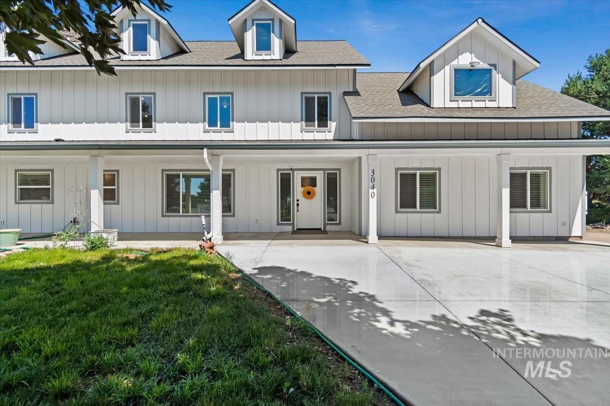 Modern farmhouse exterior with white board and batten siding, multiple dormer windows, a covered front porch, and a concrete driveway