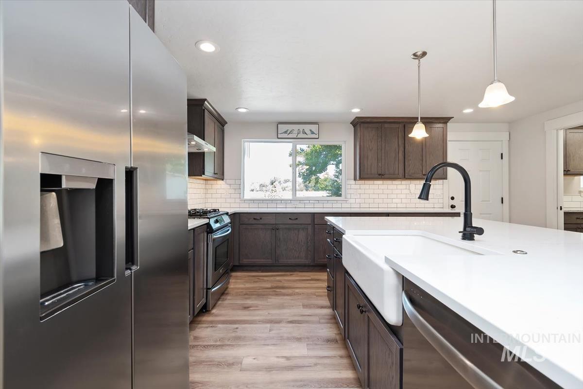 Kitchen featuring a stainless steel refrigerator, white subway tile backsplash, dark wood cabinetry, white farmhouse sink, and white countertops