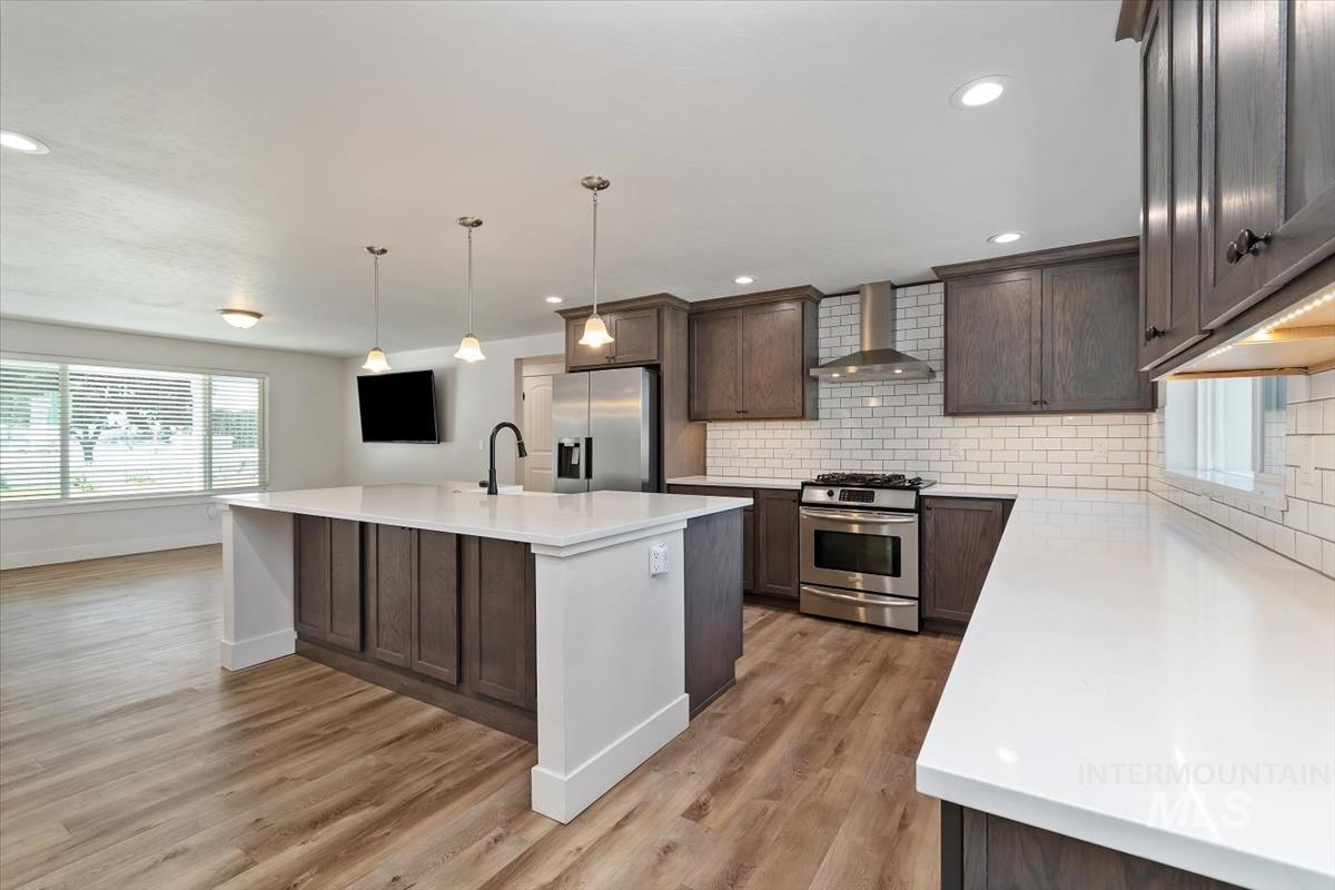 Spacious kitchen featuring an island with three pendant lights, stainless steel appliances, white subway tile backsplash, white countertops, and wood-finish flooring