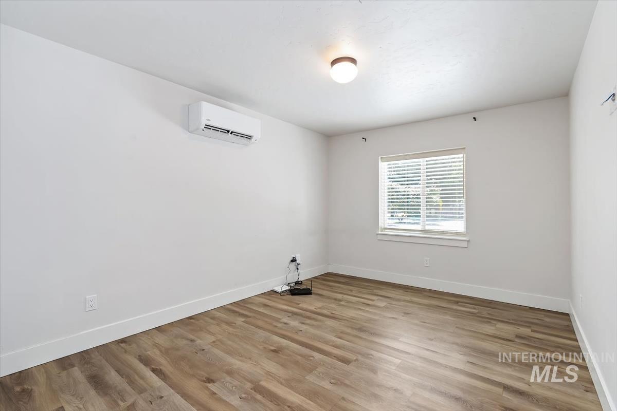 Bright interior room featuring wood-finish flooring, a window with horizontal blinds, a ceiling-mounted light fixture, and a wall-mounted mini-split HVAC unit