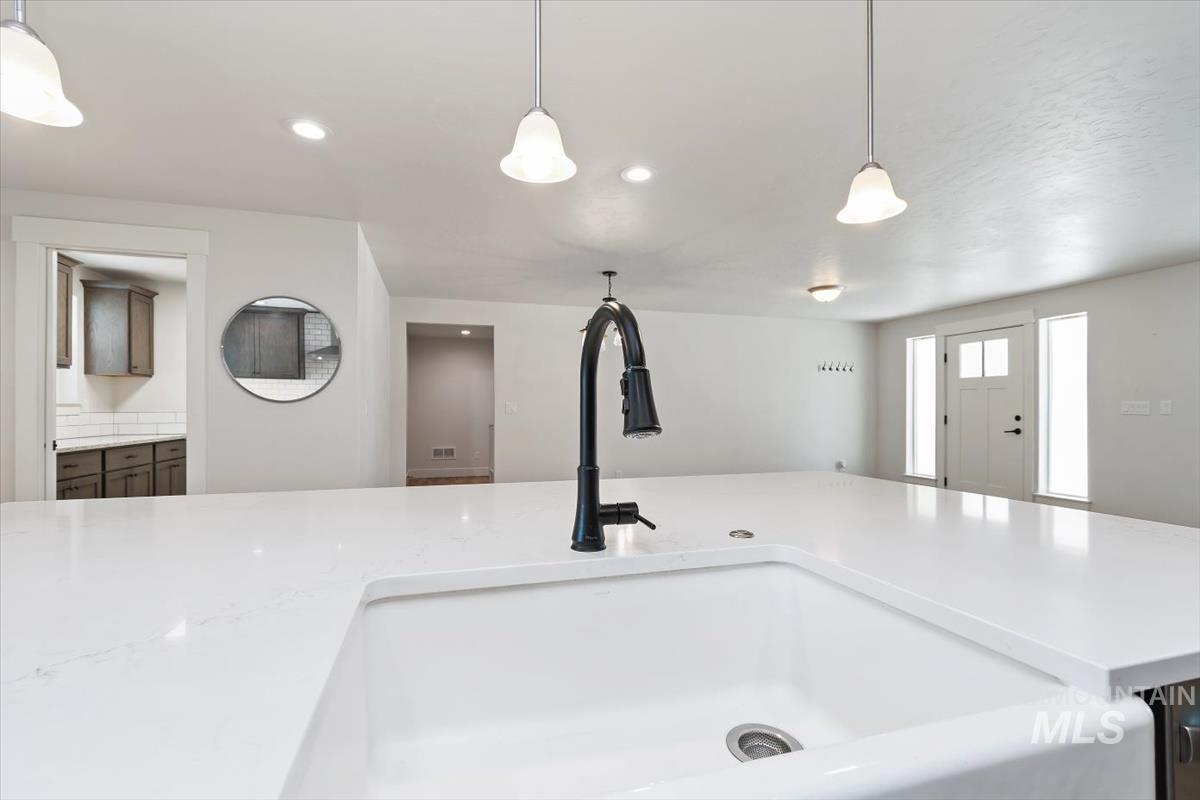Kitchen island featuring a white apron front sink, black pull-down faucet, and white countertops