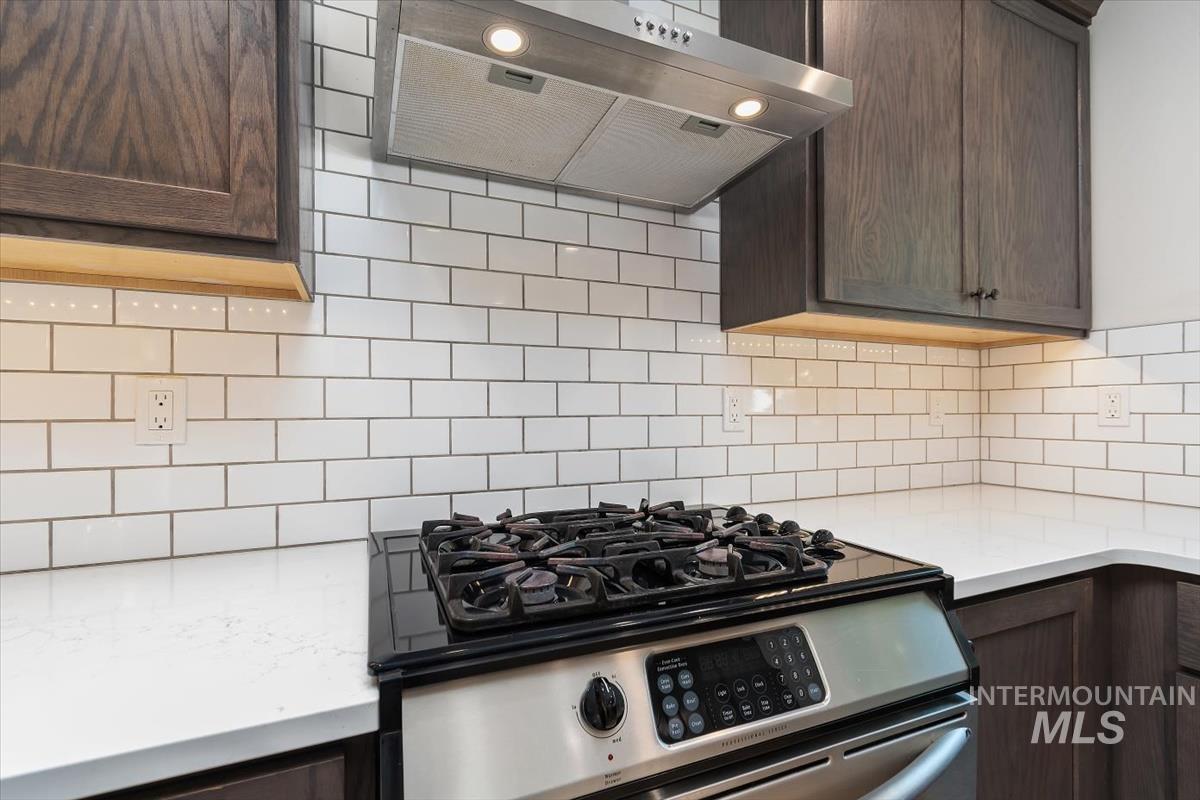 Modern kitchen featuring a stainless steel gas range, white subway tile backsplash, white countertops, and dark wood-finish cabinetry with under-cabinet lighting