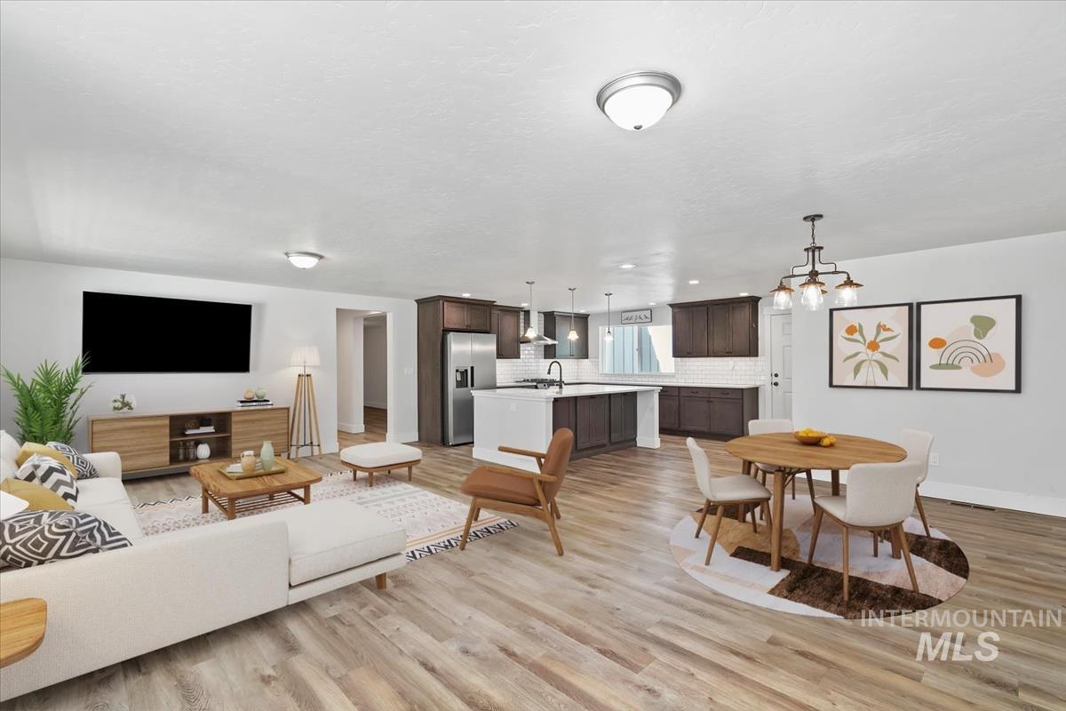 Open-concept living space featuring wood-finish flooring, a kitchen with dark cabinetry and stainless steel appliances, a white subway tile backsplash, and a central island with seating