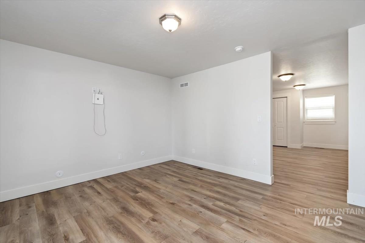 Spacious room featuring wood-finish flooring, white baseboards, and neutral wall paint
