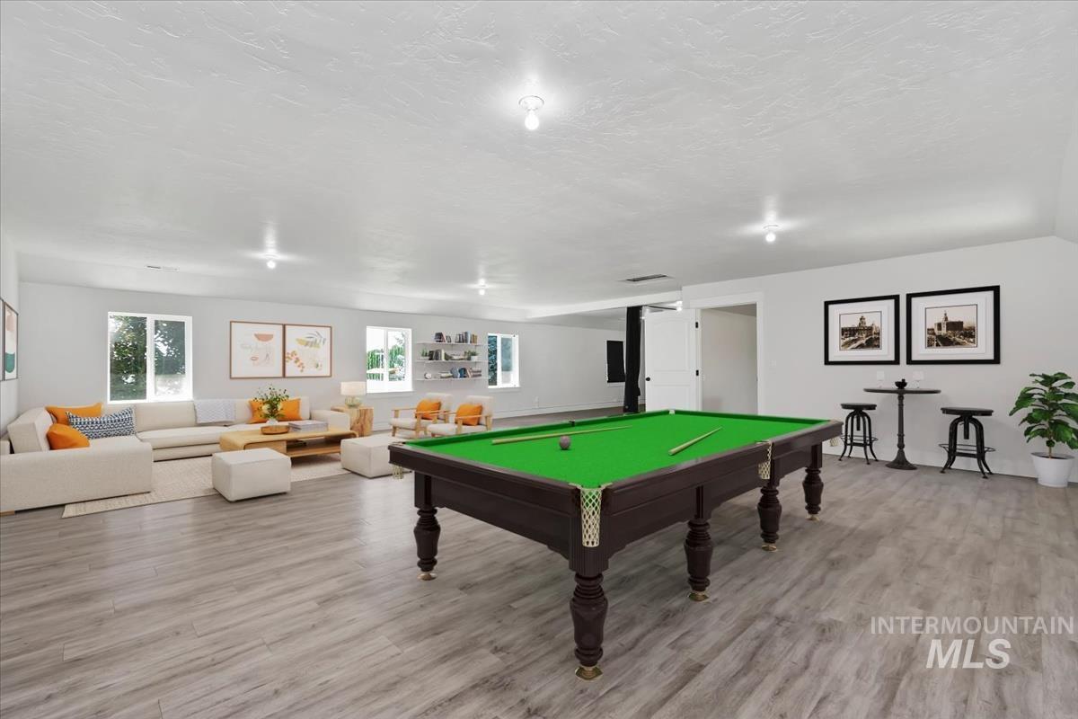 Spacious entertainment area featuring wood-finish flooring, recessed lighting, multiple windows, and a built-in shelving unit