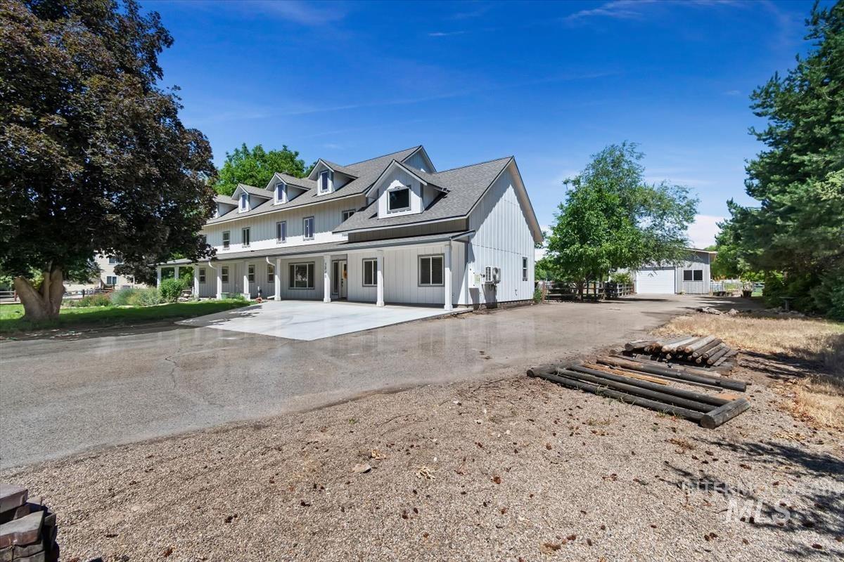 Two-story property featuring a white exterior, multiple dormer windows, a covered porch with white columns, and a paved driveway