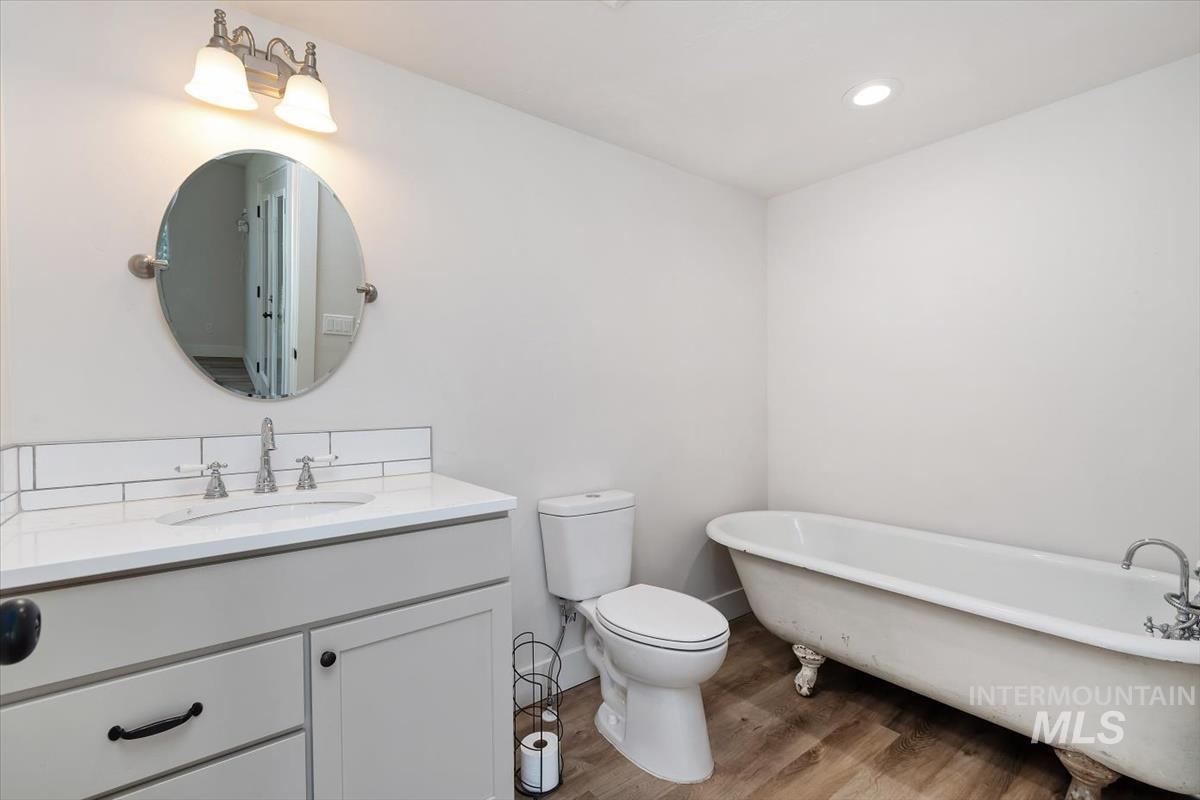 Bathroom featuring a freestanding clawfoot tub, a single vanity with a white countertop and subway tile backsplash, wood-finish flooring, and a recessed ceiling light