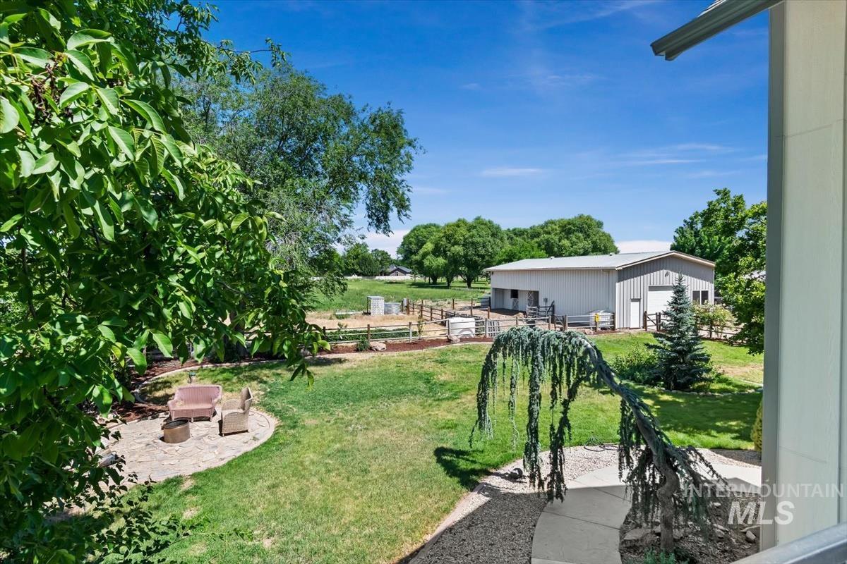 Expansive outdoor area featuring a stone patio, manicured lawn, gravel pathway, mature trees, and a distant outbuilding