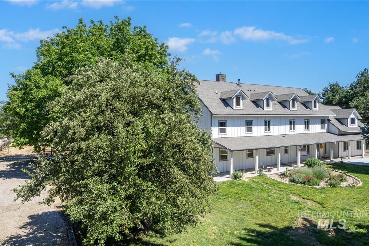 Expansive property featuring a white-sided residence with multiple dormer windows, a full-length covered porch with white columns, and a gravel driveway