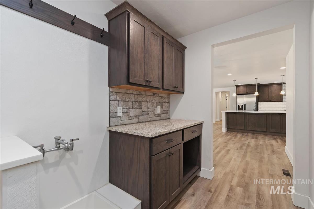 Laundry area featuring dark wood-finish cabinetry with granite-style countertops, stone-look tile backsplash, and a utility sink with wall-mounted faucet
