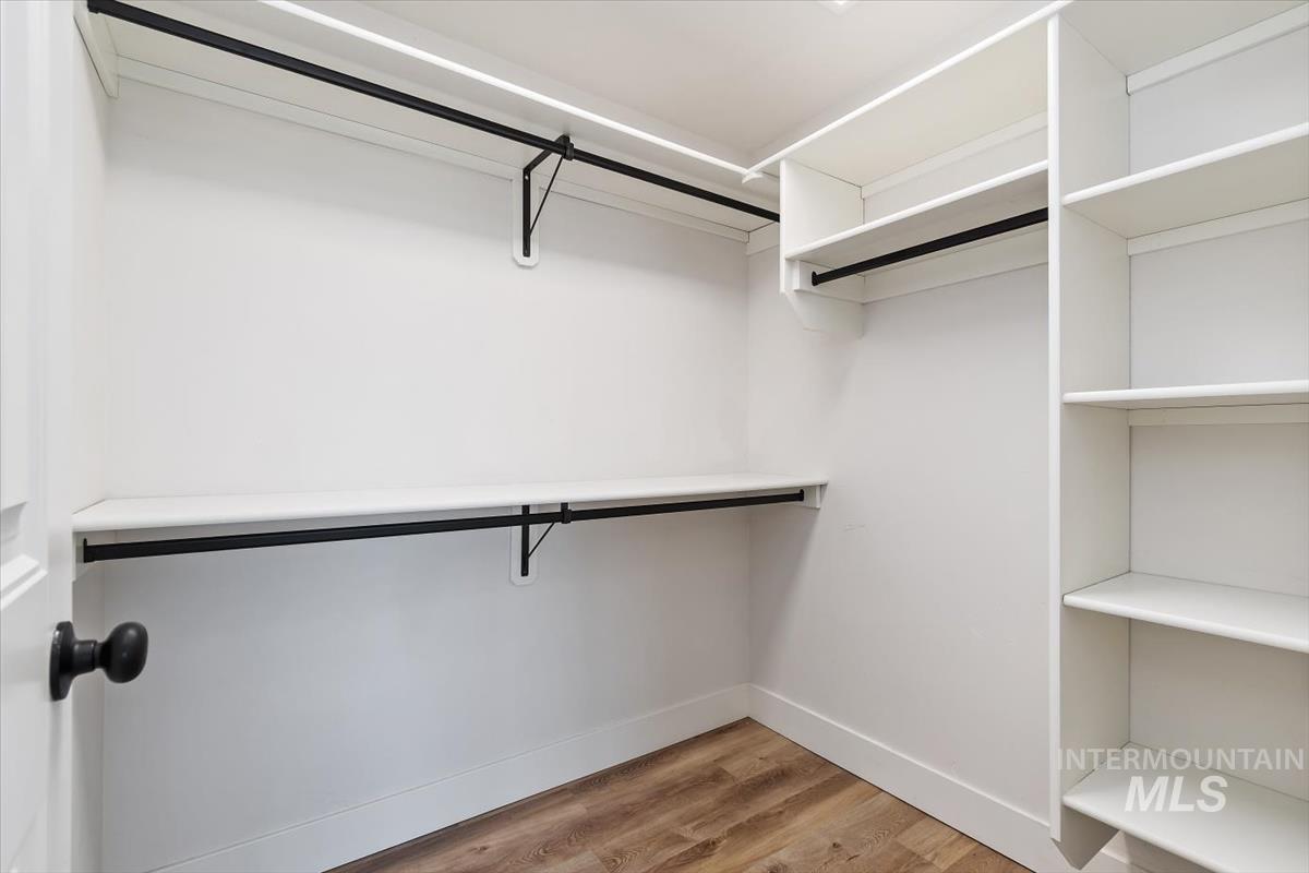 Walk-in closet featuring white built-in shelving, two black hanging rods, a white shelf, and wood-finish flooring