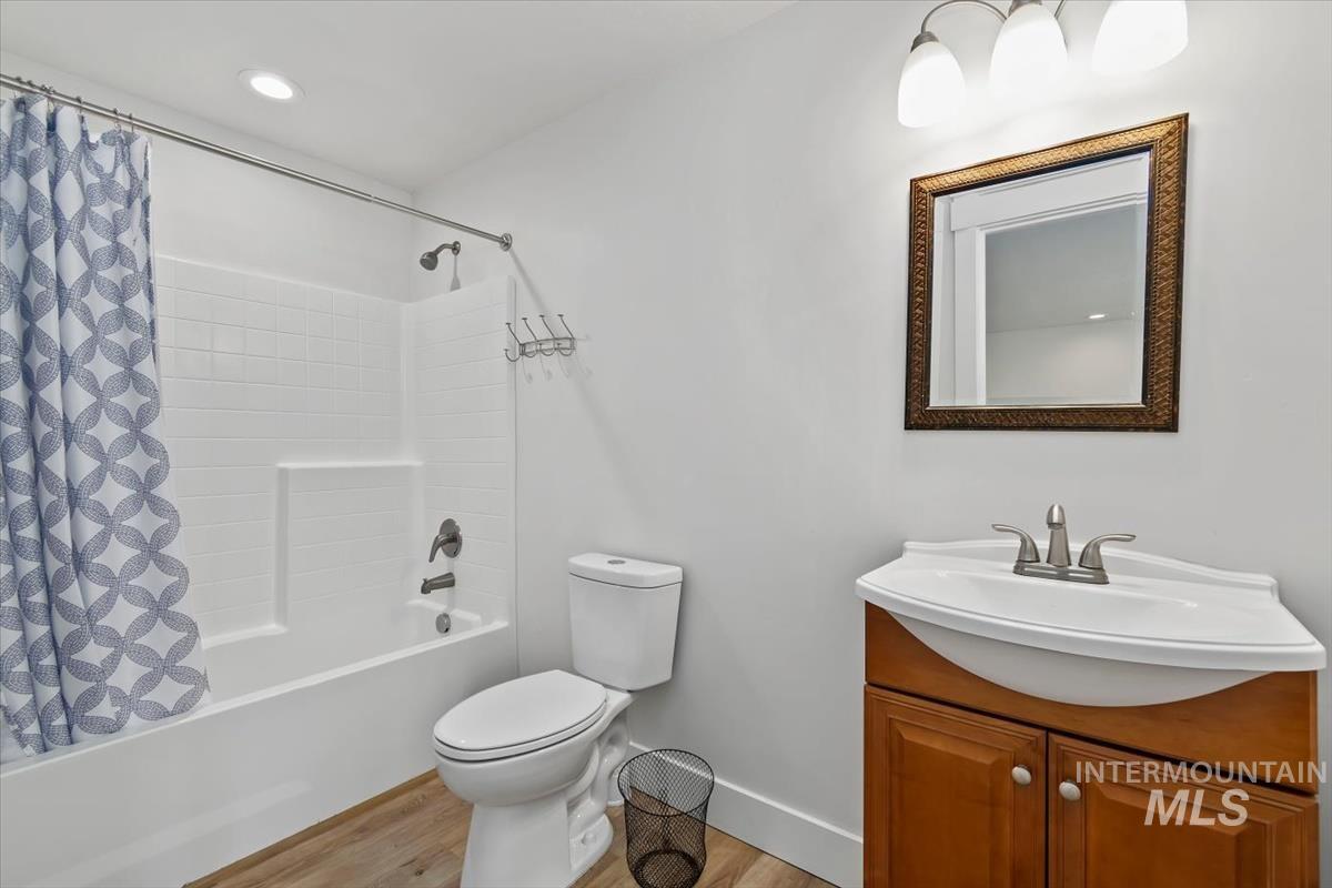 Bathroom featuring a bathtub with subway tile surround, a toilet, a vanity with an integrated sink, a framed mirror, and wood-finish flooring