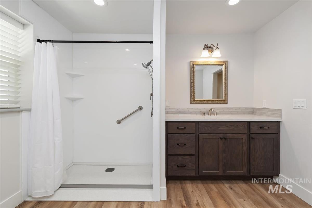 Bathroom featuring a white shower stall with a grab bar, a dark wood-finish vanity with a light-toned countertop, and wood-finish flooring