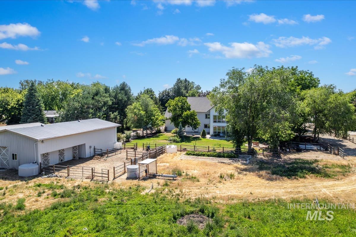 Expansive property featuring a white barn with multiple stalls, fenced enclosures, and mature trees