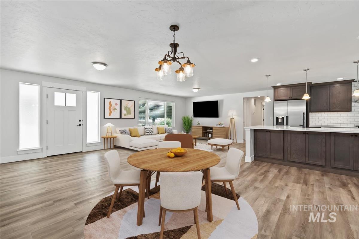 Open-concept interior featuring wood-finish flooring, a white paneled front door with frosted sidelights, a kitchen island with dark cabinetry, stainless steel appliances, and a white subway tile backsplash