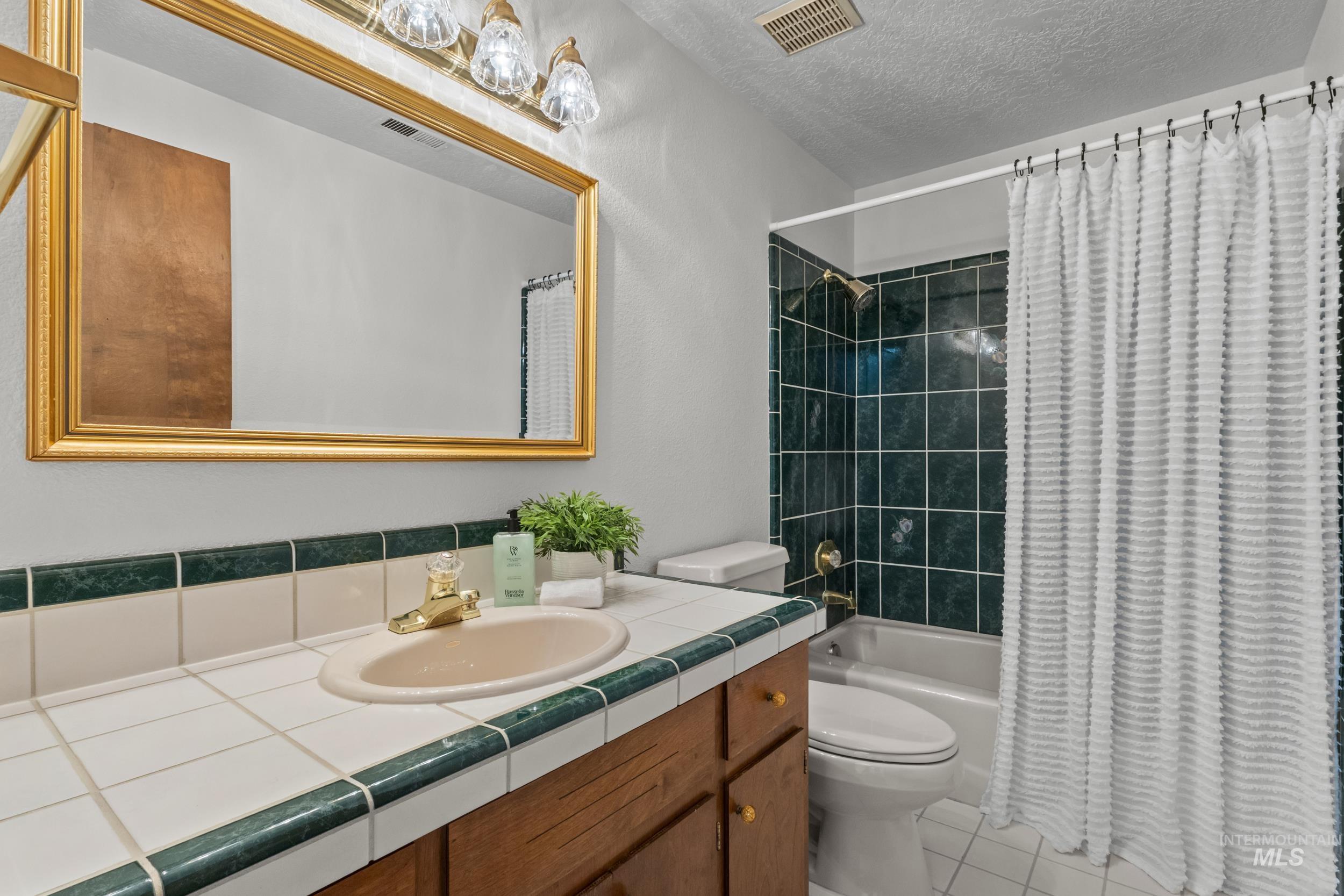 Full bathroom with shower / bath combo, vanity, a textured ceiling, and light tile patterned flooring
