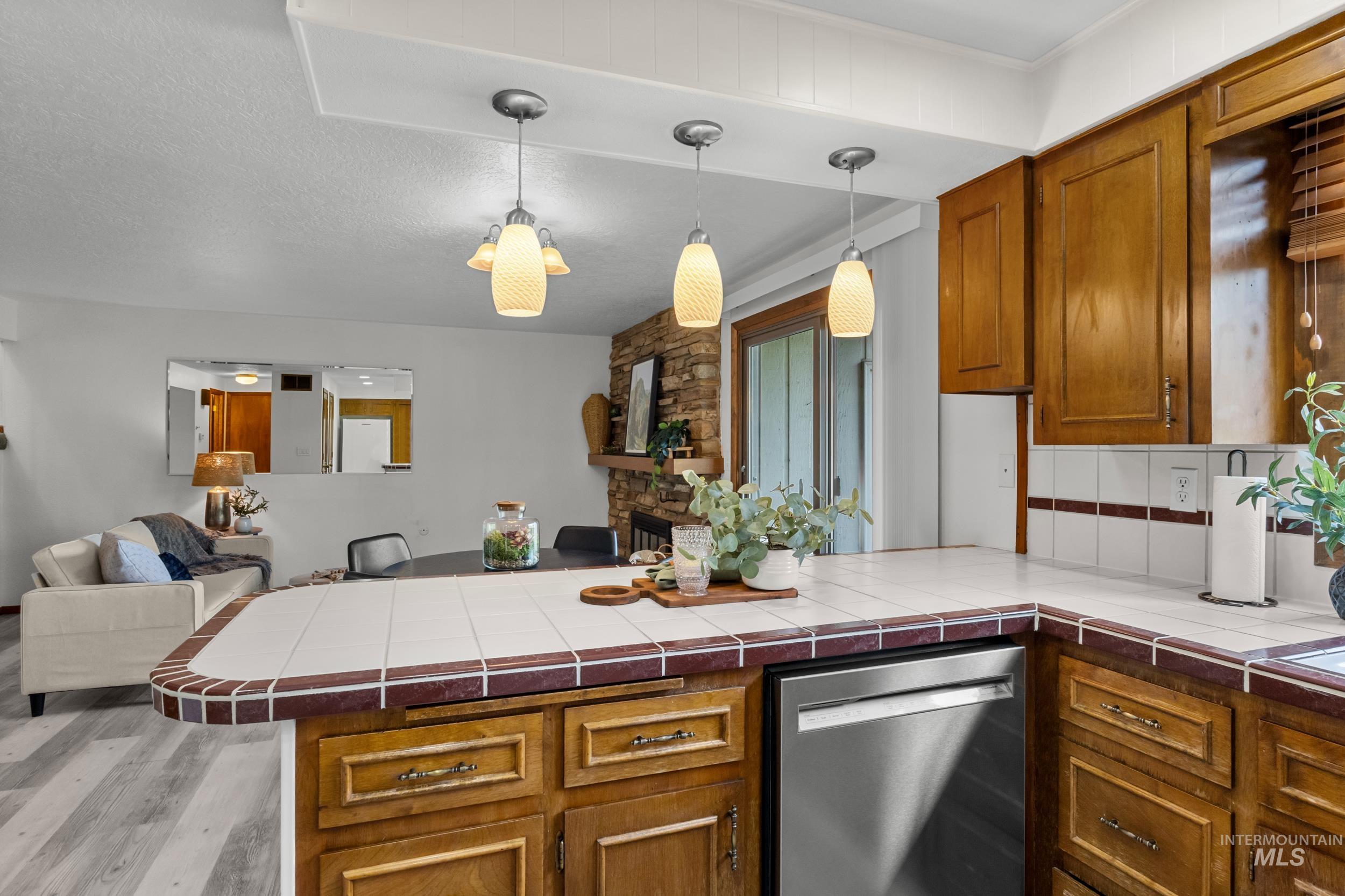 Kitchen featuring open floor plan, brown cabinets, dishwasher, a peninsula, and tile counters