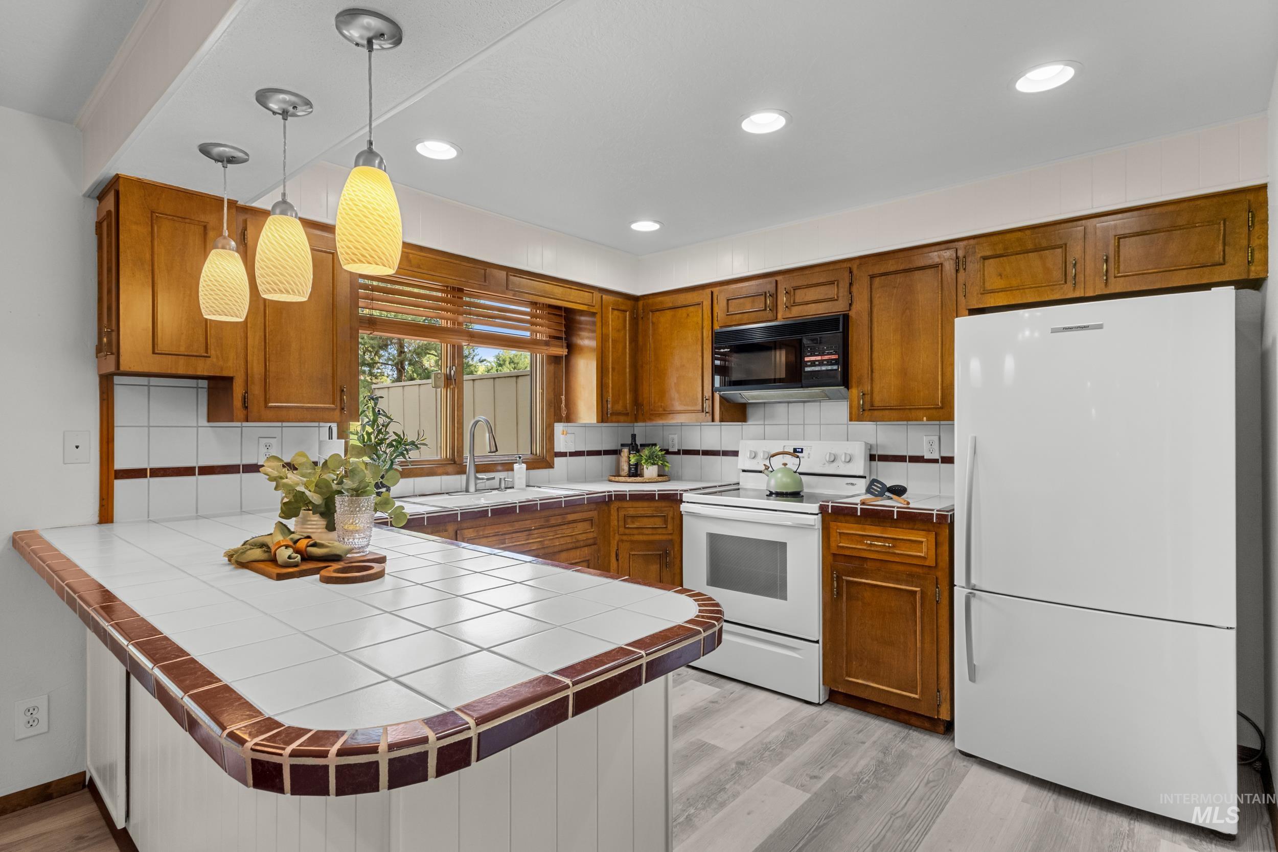 Kitchen with tile countertops, a peninsula, brown cabinetry, and recessed lighting