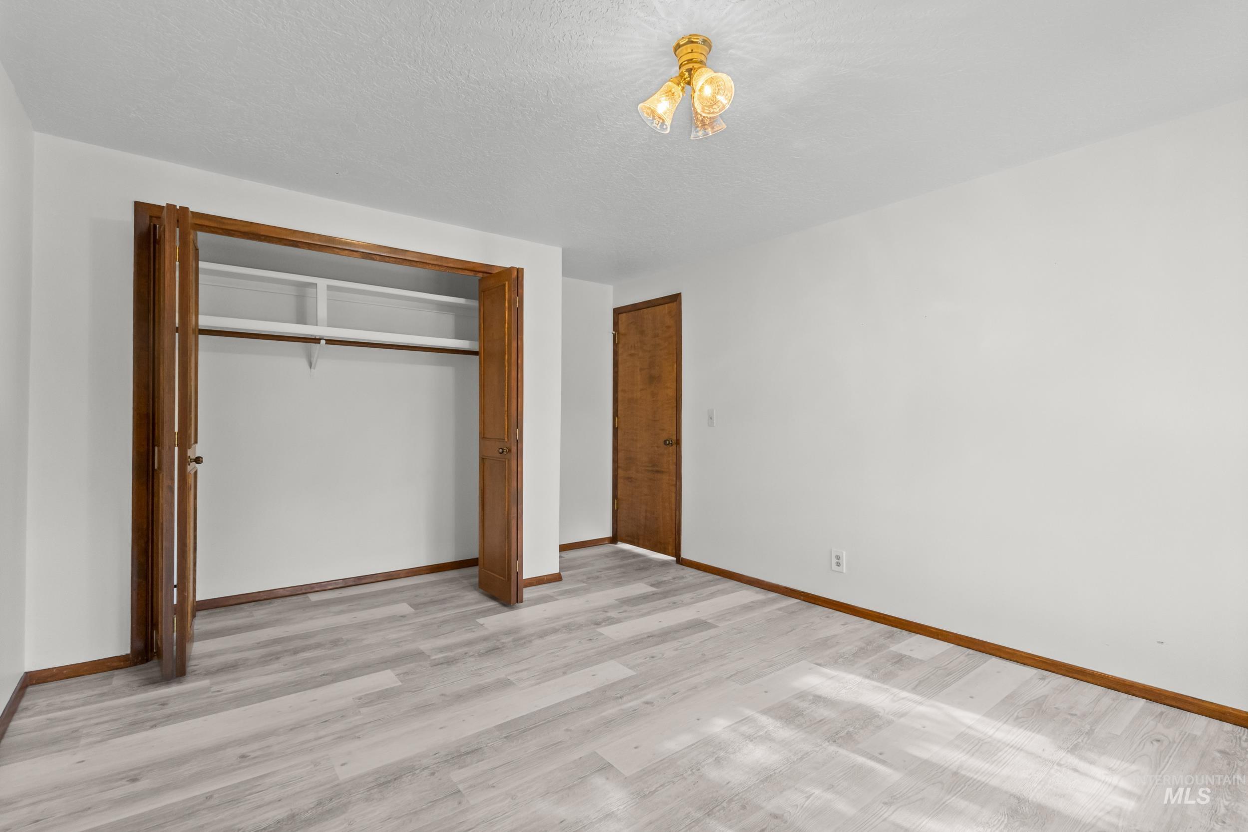 Unfurnished bedroom featuring light wood finished floors, a closet, and a textured ceiling
