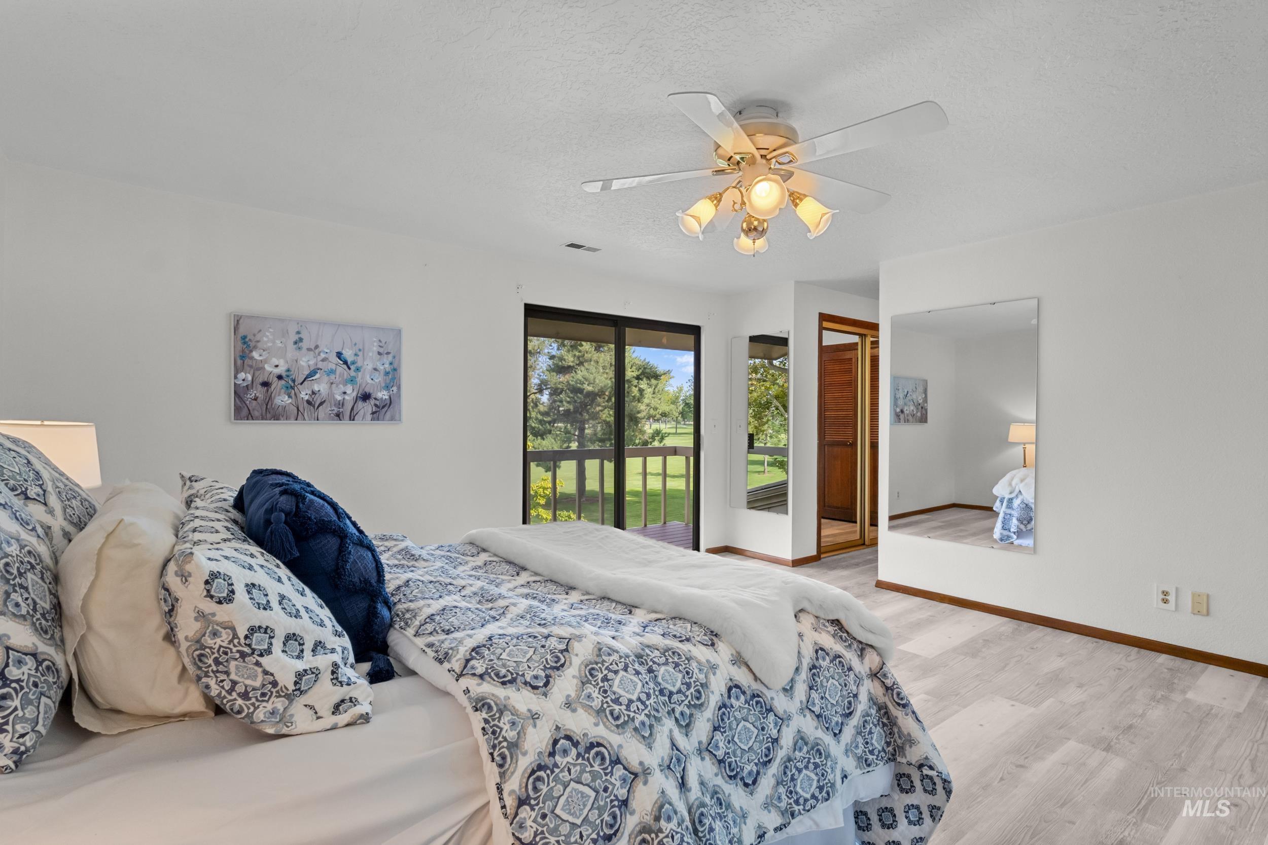 Bedroom featuring light wood finished floors, access to exterior, a textured ceiling, and a ceiling fan