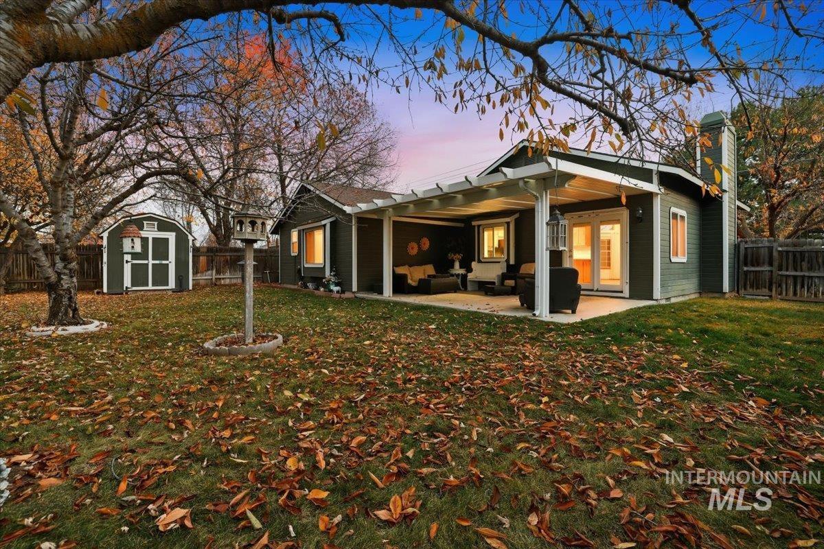 Back of property at dusk featuring a fenced backyard, a storage unit, a chimney, and a patio area
