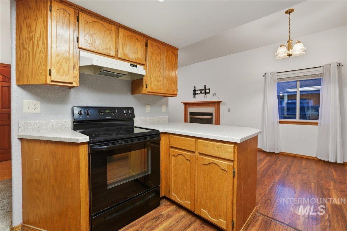 Kitchen featuring a peninsula, black range with electric stovetop, light wood-type flooring, light countertops, and under cabinet range hood