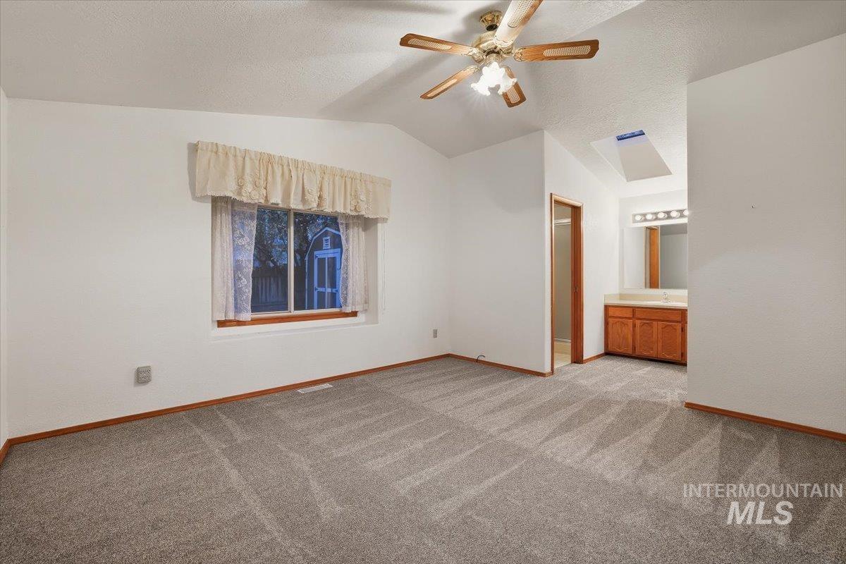 Unfurnished bedroom with lofted ceiling, light colored carpet, a ceiling fan, connected bathroom, and a textured ceiling