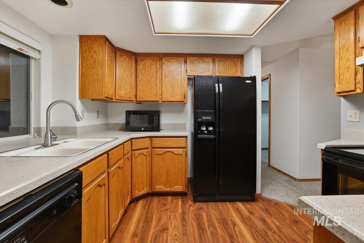 Kitchen featuring light wood-style flooring, black appliances, light countertops, and brown cabinets