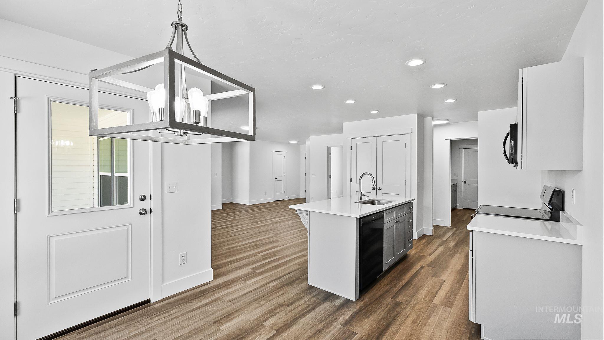 Kitchen with a chandelier, recessed lighting, dark wood finished floors, a center island with sink, and black appliances