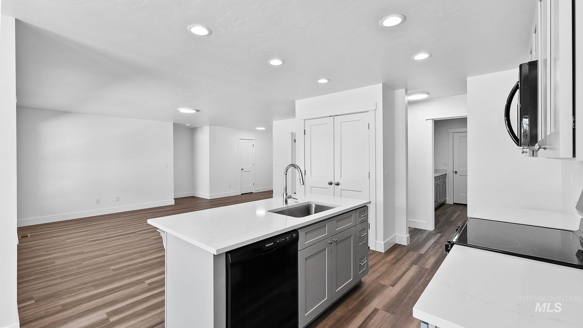 Kitchen with dark wood-style flooring, black appliances, gray cabinetry, recessed lighting, and a center island with sink