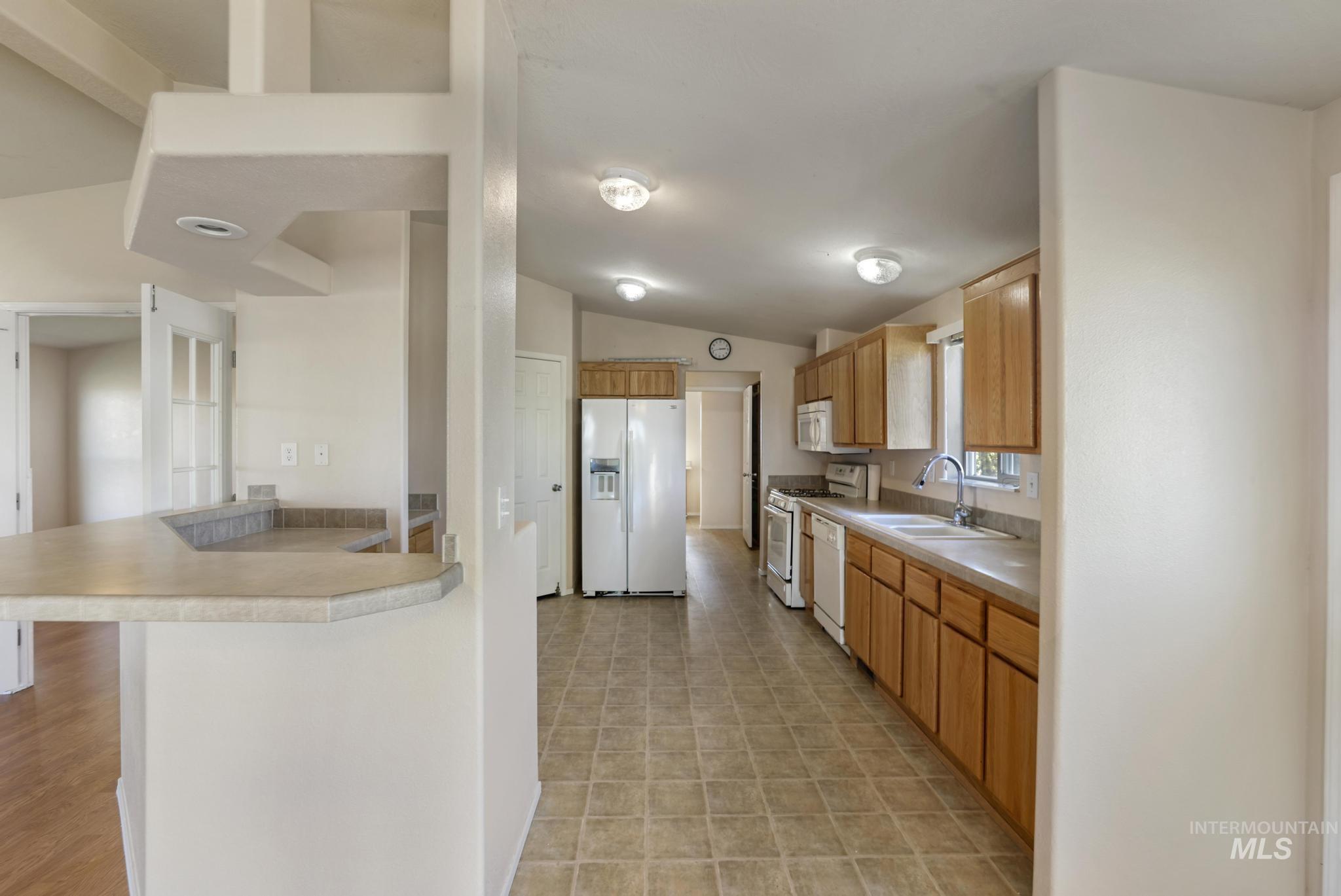 Kitchen featuring light countertops, white appliances, vaulted ceiling, a breakfast bar, and a peninsula